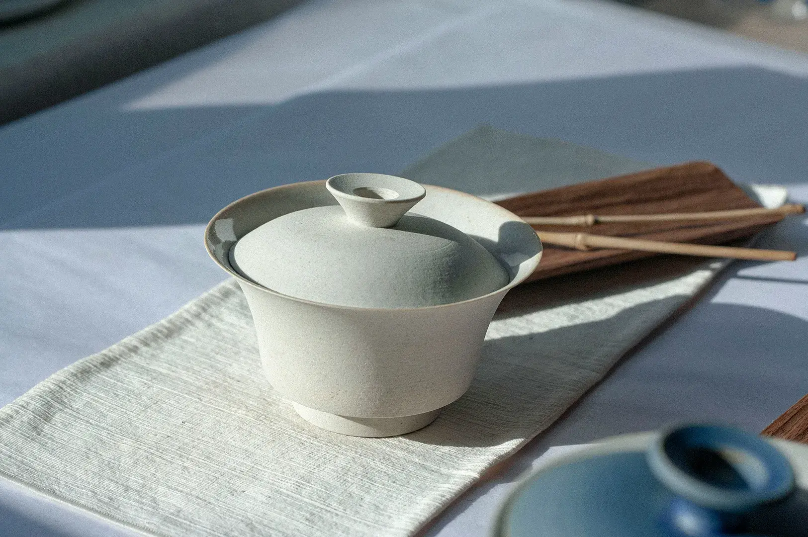 Matte off-white ceramic gaiwan on a linen table runner.