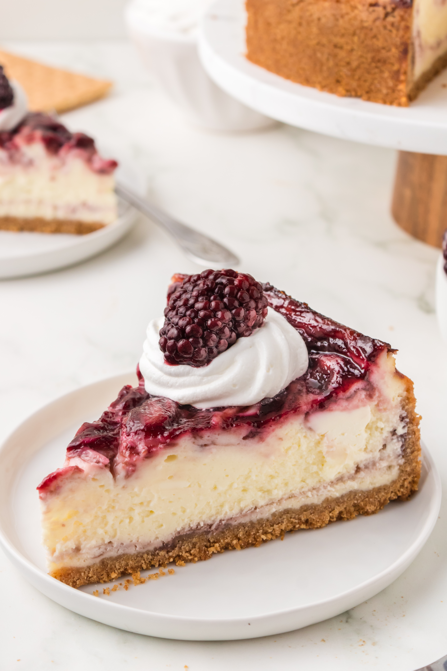 slice of blackberry cheesecake with graham cracker crust topped with whipped cream