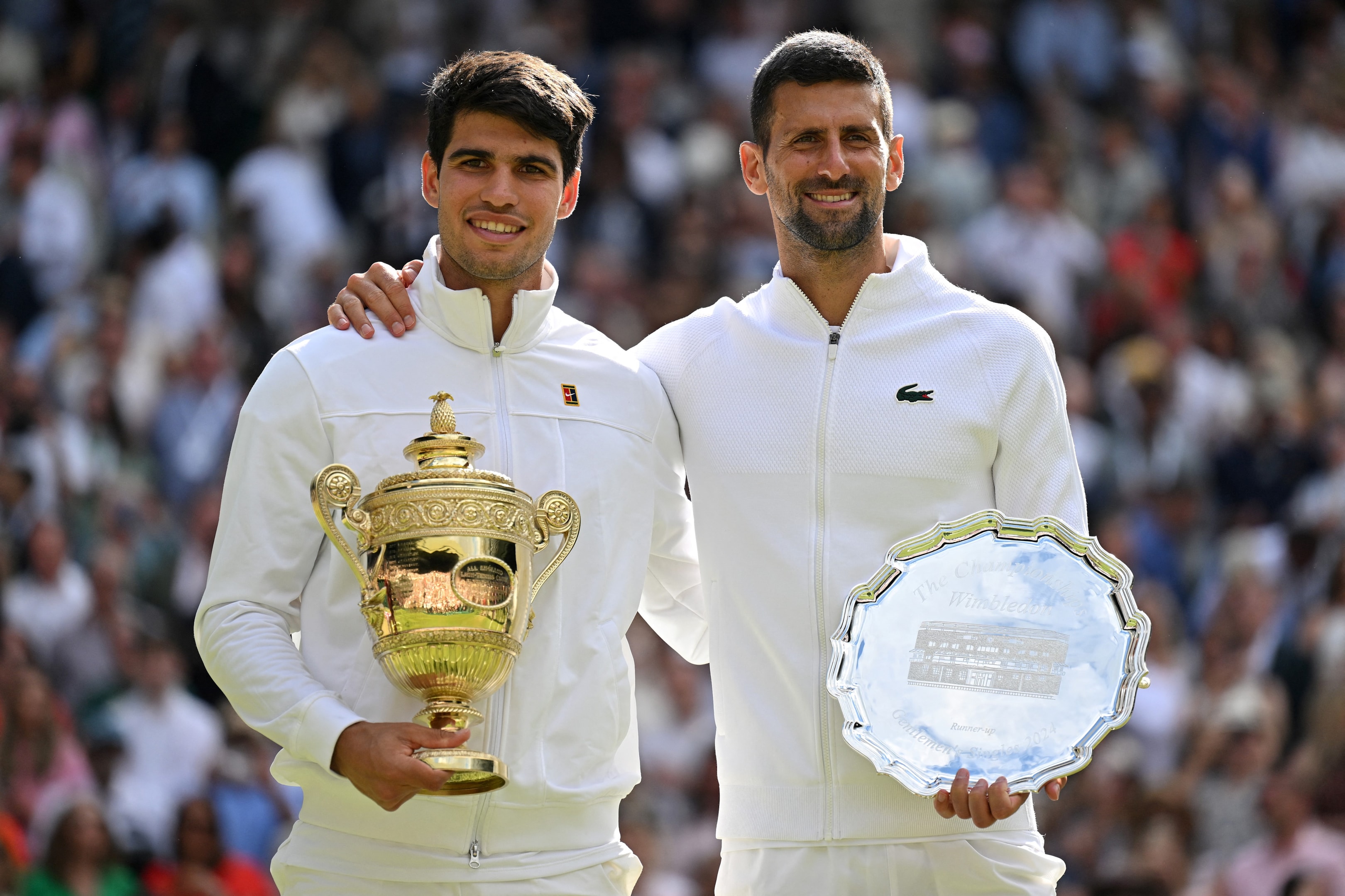 Spain's Carlos Alcaraz holding the winner's trophy with Serbia's Novak Djokovic as they pose for pictures during the men's singles final tennis match the 2024 Wimbledon Championships.