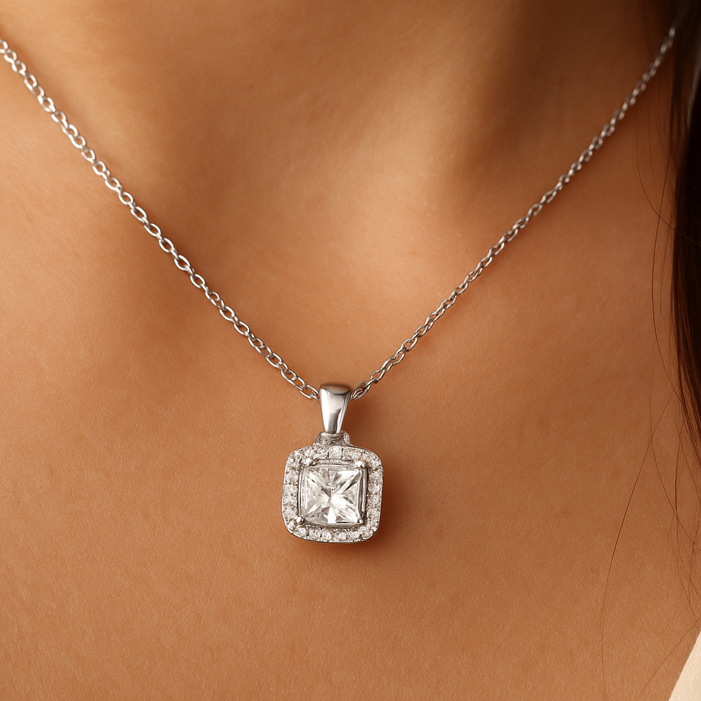 Stilingos moters kaklą puošia balto aukso pakabukas su Princess pjūvio deimantu, apsuptu mažesnių briliantų halo dizaino rėmeliu, pakabintas ant subtilios grandinėlės
