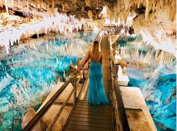 woman in a long blue dress on a wooden walkway through a crystal cave