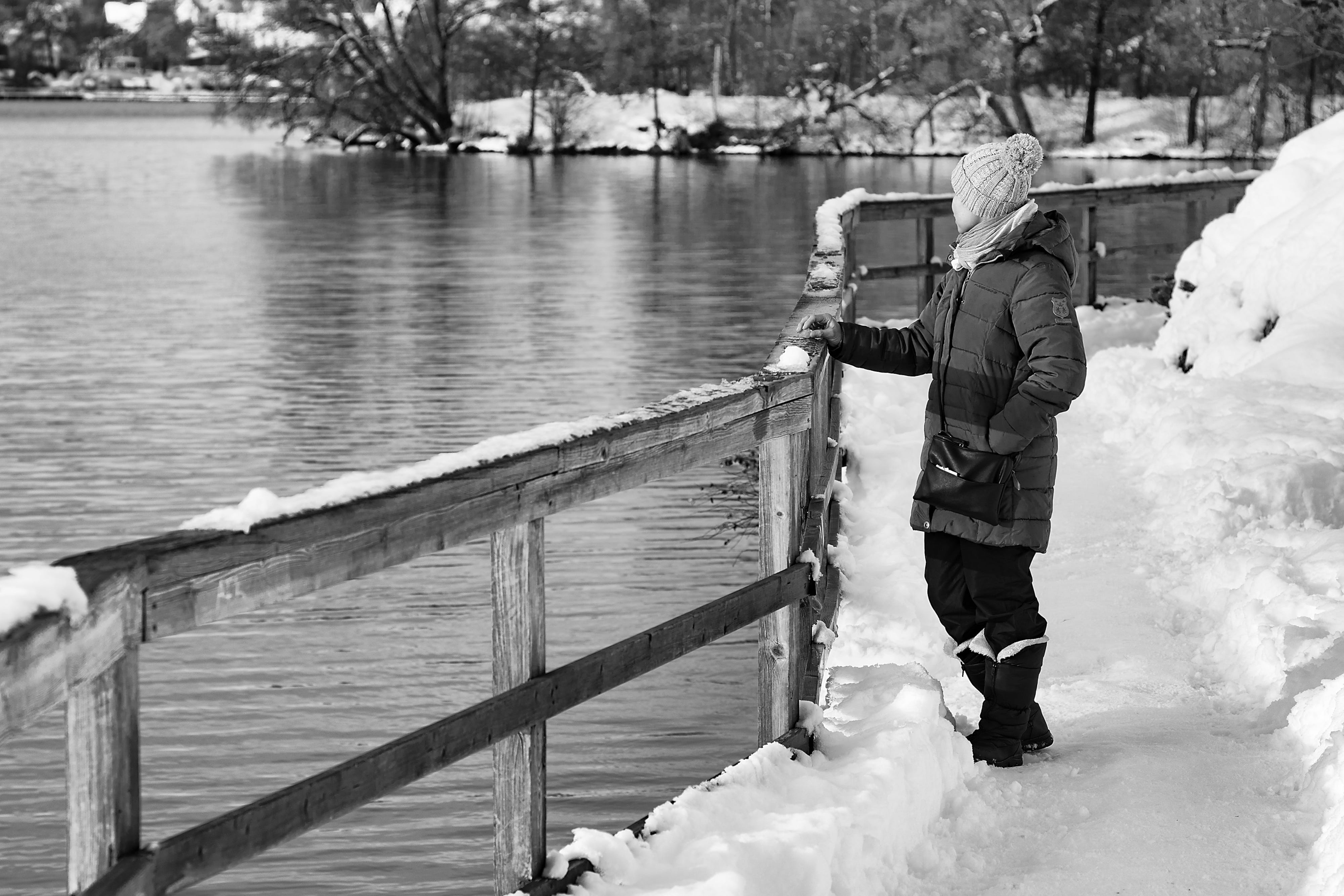 black and white photo of an individual standing and looking over a body of water in the middle of winter 