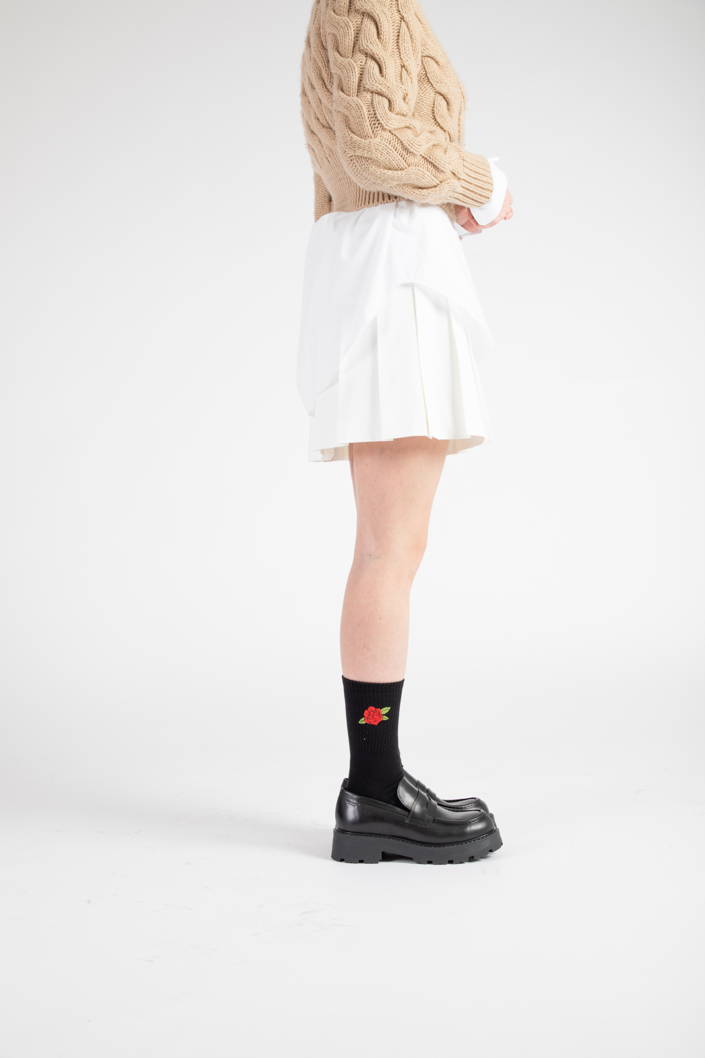 A female model wears black leather loafers with a pair of black crew socks with a red rose embroidered.