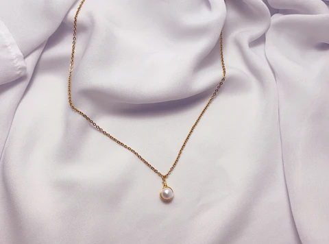 A single-pearl necklace elegantly laid out on a nicely folded light pink cloth, showcasing most of the necklace.