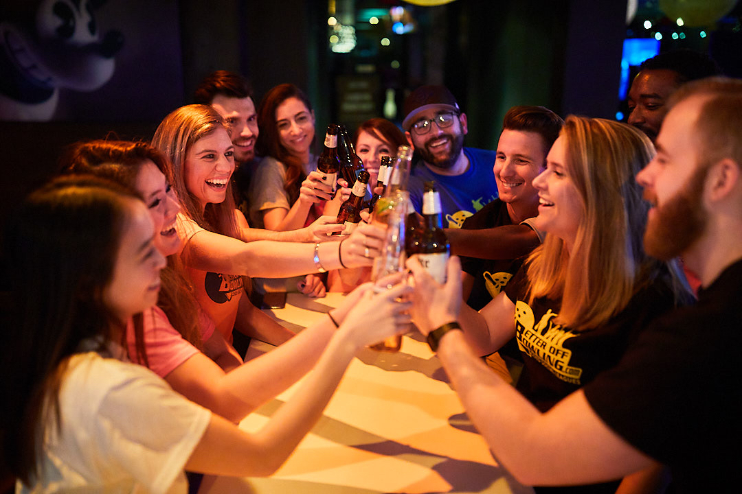 A group clinking beer bottles at Lucky Strike Bowling, one of the best corporate event ideas 