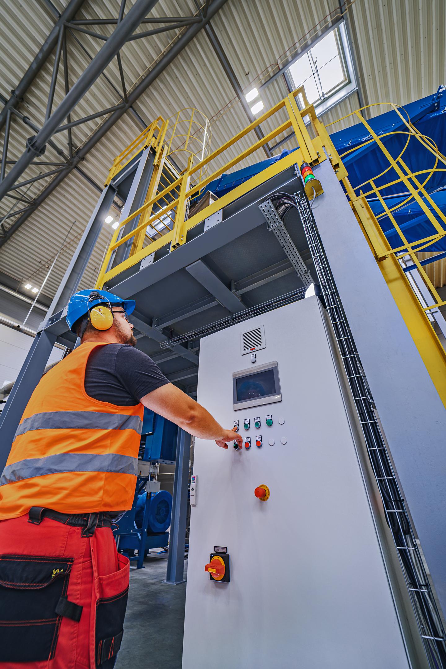 Na zdjęciu znajduje się nowoczesna hala produkcyjna zakładu recyklingu tworzyw sztucznych, w której widoczne są taśmy sortujące oraz kontenery wypełnione kolorowymi granulatami. Proces recyklingu odpadów w tym obiekcie przyczynia się do ochrony środowiska naturalnego i efektywnego gospodarowania zasobami naturalnymi.