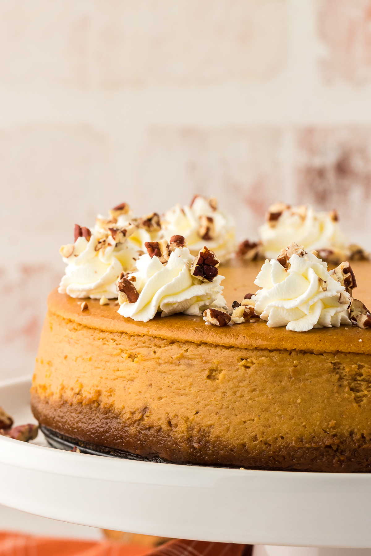 whole baked pumpkin cheesecake on a cake stand topped with homemade whipped cream and pecans