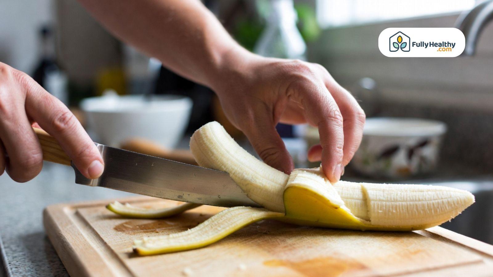 Hand slicing a banana on a wooden cutting board in a kitchen.