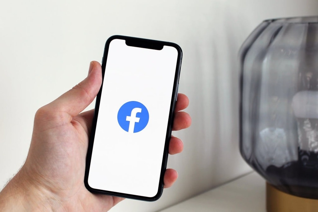 A Person holding an iPhone with the Facebook logo on-screen