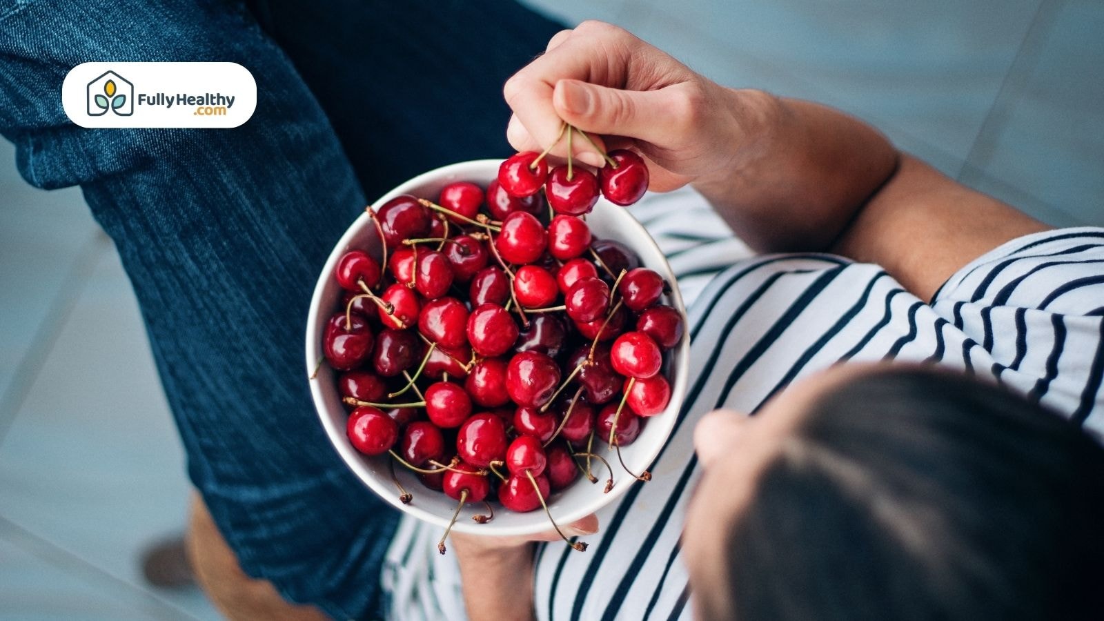 Person holding a bowl of fresh cherries while picking cherries