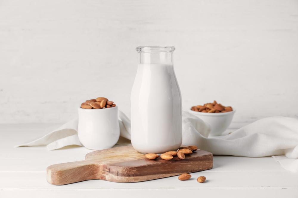 Almond milk in a glass container surrounded by bowls of whole almonds. 