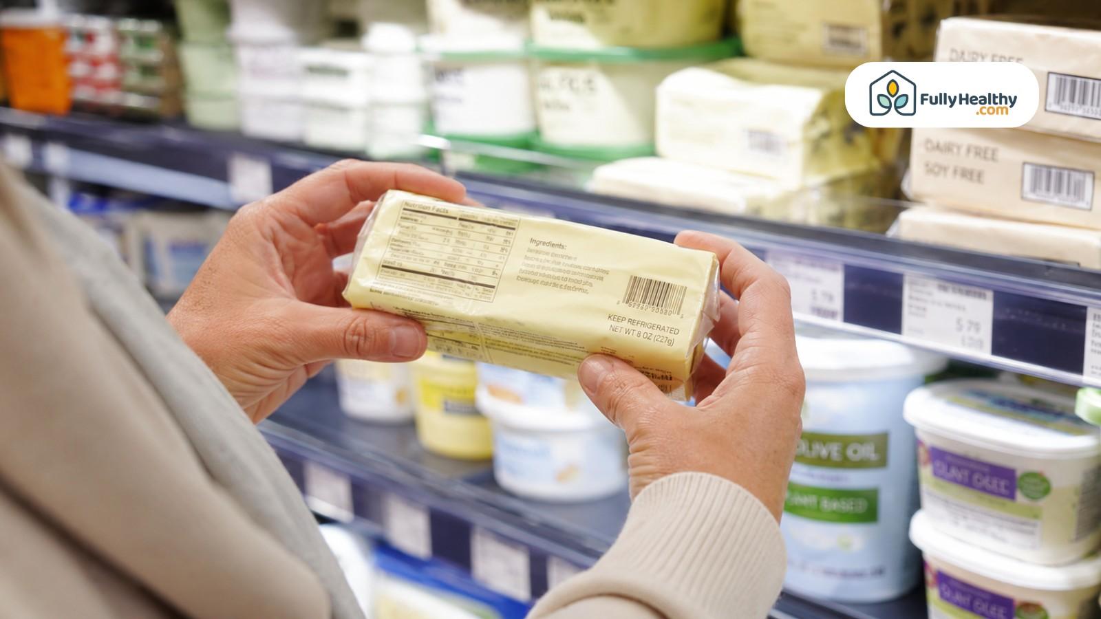 Shopper reading butter ingredient label beside dairy-free spread alternatives in refrigerated grocery aisle
