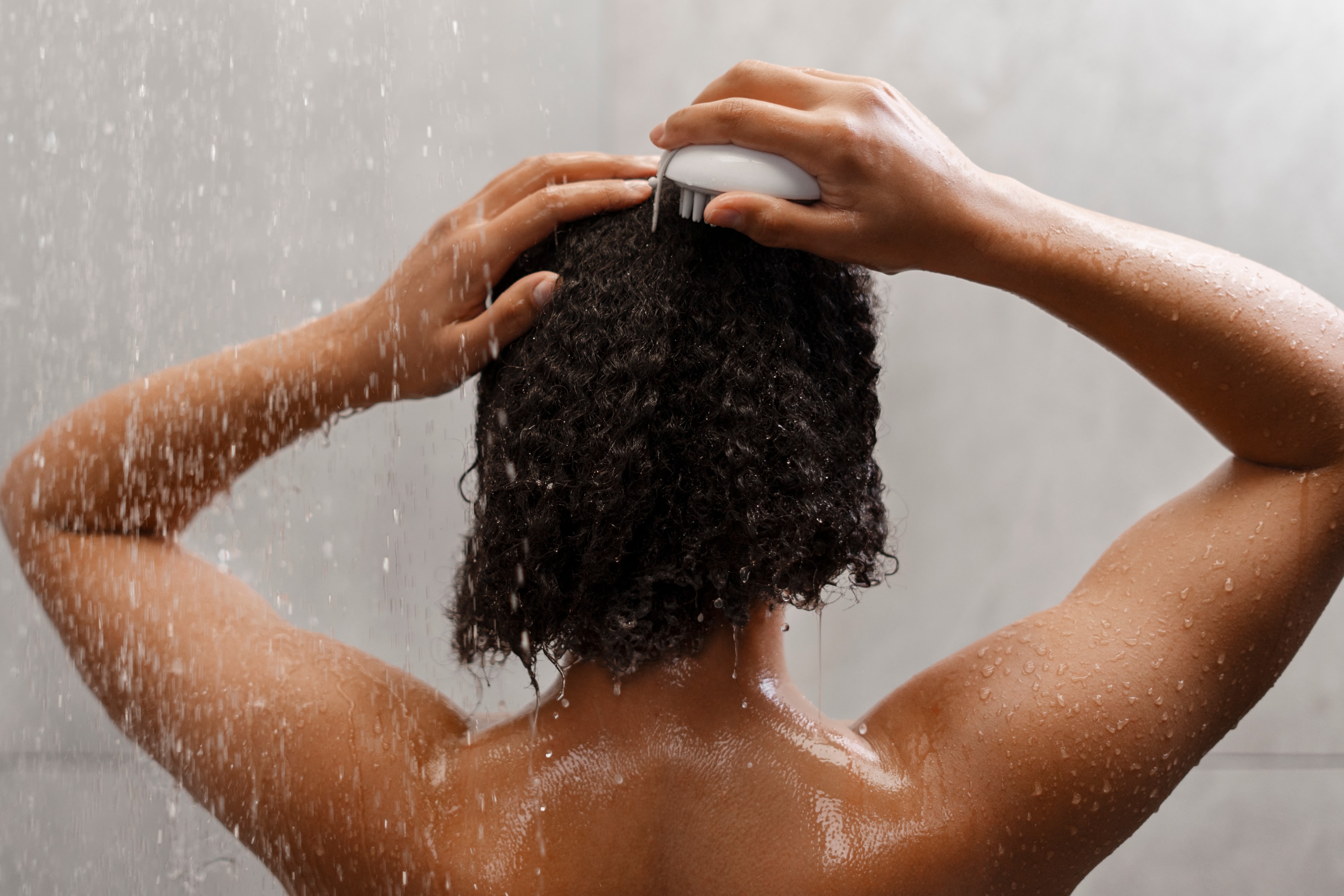 a woman brushing her natural curls while taking a shower