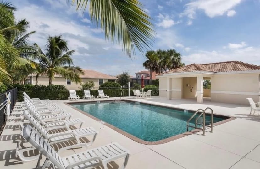 The image depicts a sparkling community pool surrounded by lounge chairs and lush tropical landscaping, creating a peaceful retreat for residents in the gated community of Banyan Bay in Fort Myers, FL. The inviting cabana area enhances the outdoor amenities, making it an ideal spot for relaxation and enjoyment.