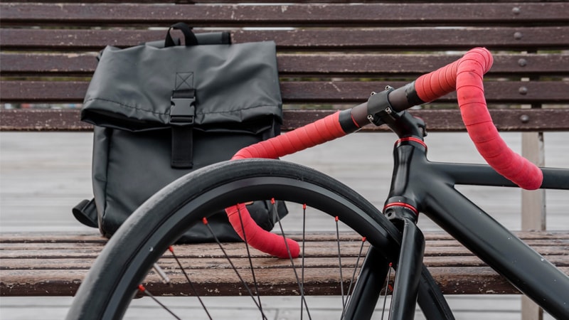 black ride bike with red handle parked against a maroon bench with a black bag.