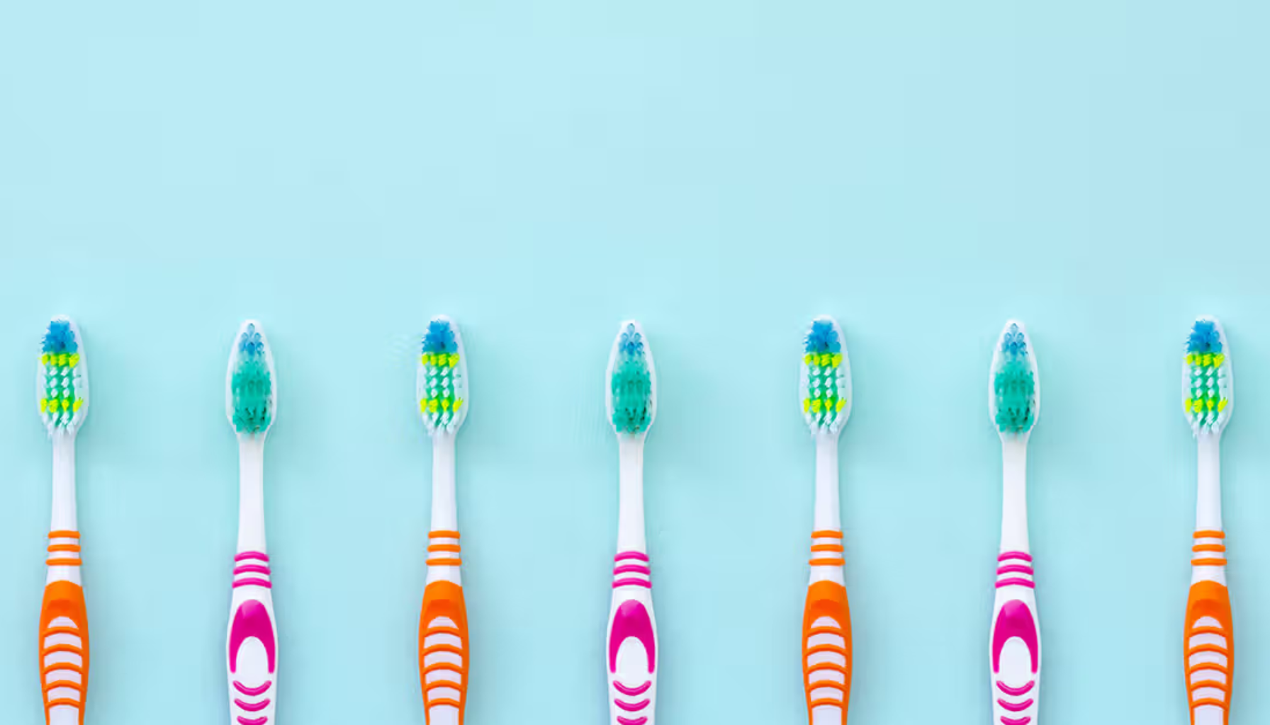 Hvor ofte bør du bytte tannbørste? Ekspertenes anbefaling 13 Seks fargerike tannbørster med ulike bustmønstre står oppreist på en lyseblå bakgrunn i jevn avstand.