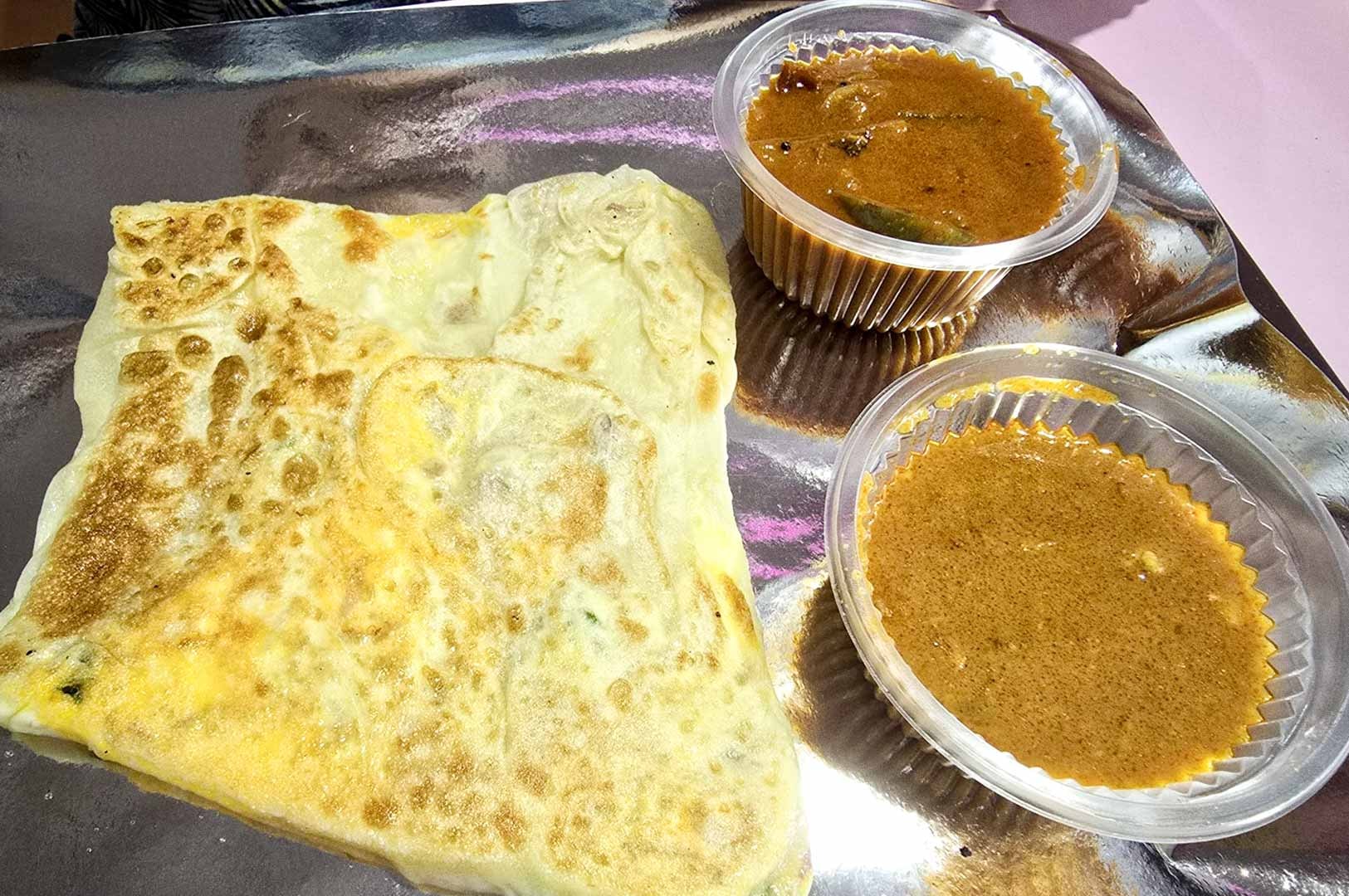 A serving of roti prata on a metal tray accompanied by two small containers of curry.