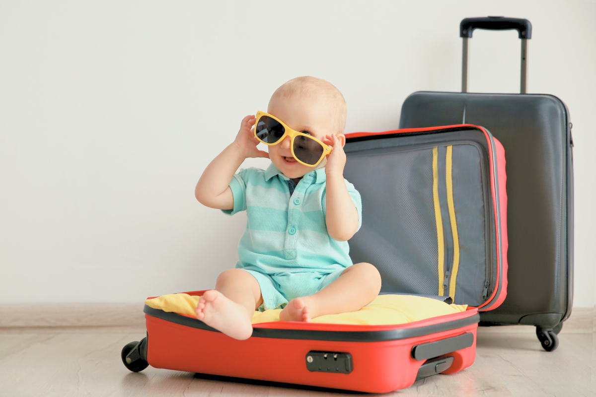 Baby Boy sitting on top of open suitcase. Poppyseed Play