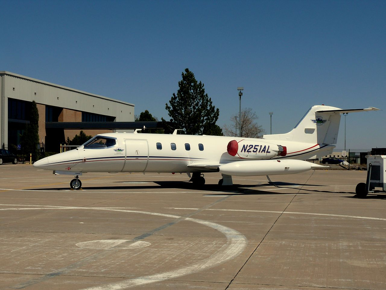 Learjet 25 parked on tarmac at an airport by some hangars.