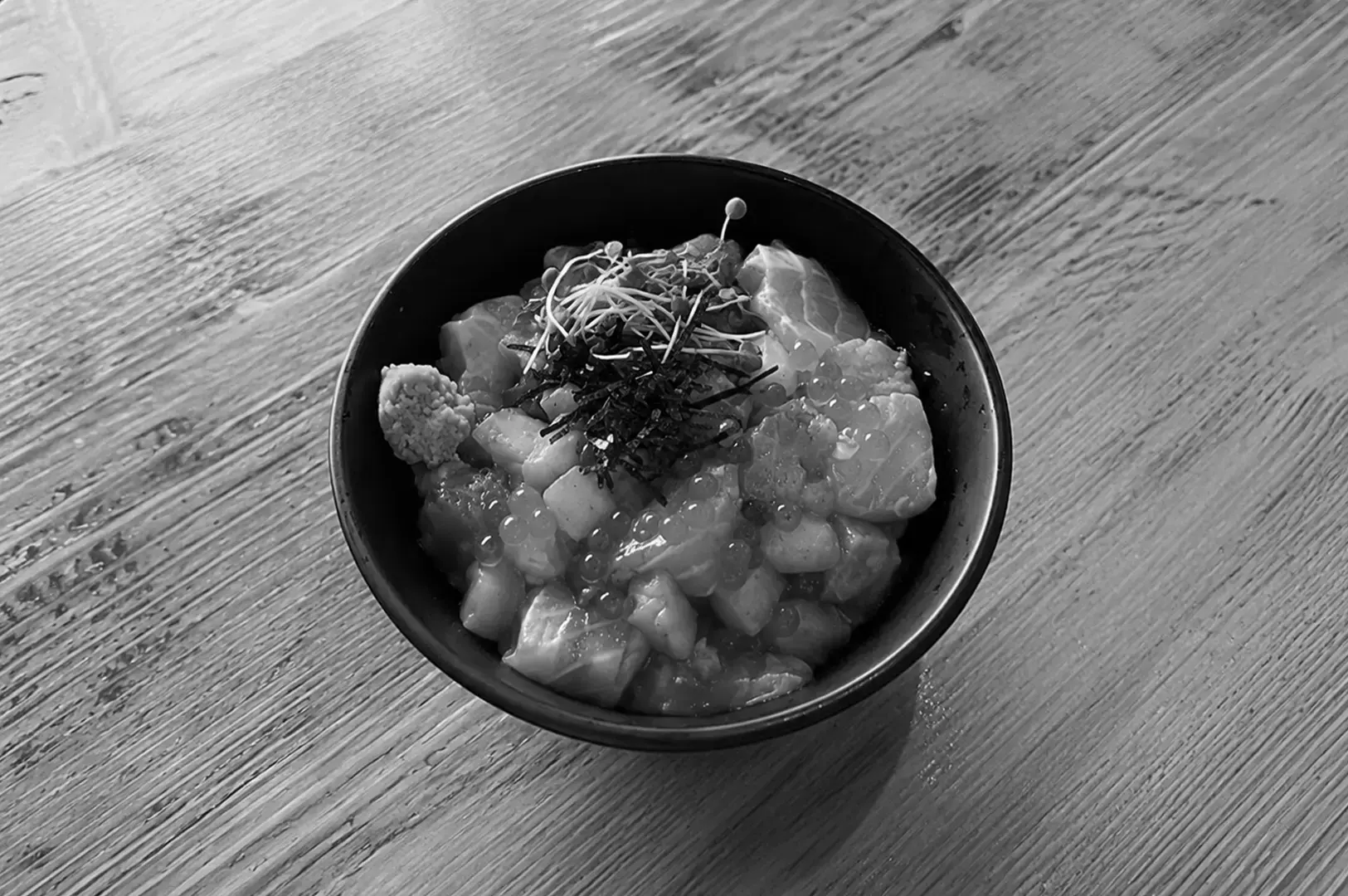 Teppei Syokudo kaisen don with diced salmon, sashimi cubes, ikura, tobiko, and sprouts served in a black bowl.