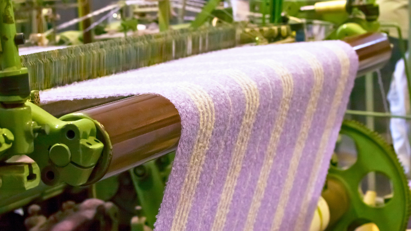 A close-up of a loom weaving striped fabric in different shades.