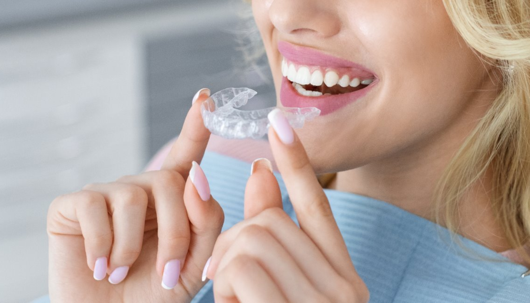 Kvinne med langt blondt hår smiler mens hun holder en gjennomsiktig tannskinne klar til å sette inn.
