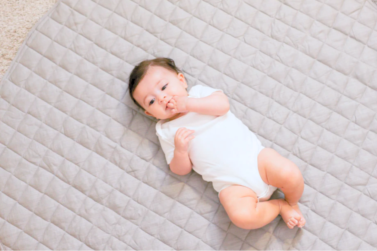 Baby doing floor time on a gray play mat by Poppyseed Play