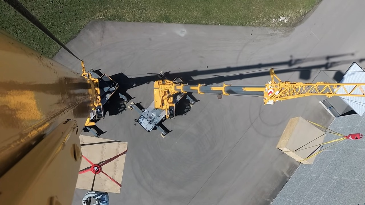 Aerial view of a mobile crane operating on a construction site, lifting heavy equipment with a dynamic shadow casting on the ground, illustrating industrial machinery in action