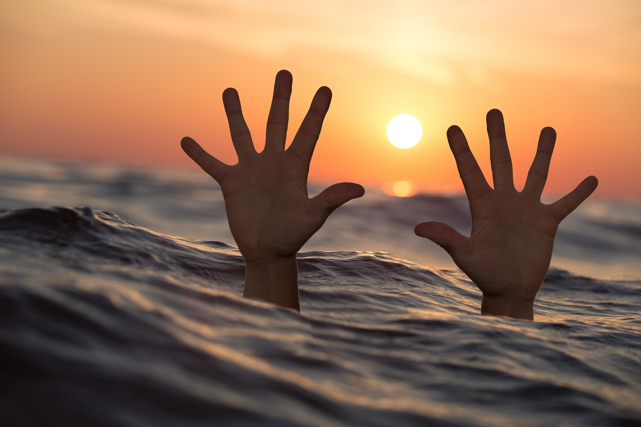 Two hand above the ocean surface against the sunset depicting how to get out of survival mode 