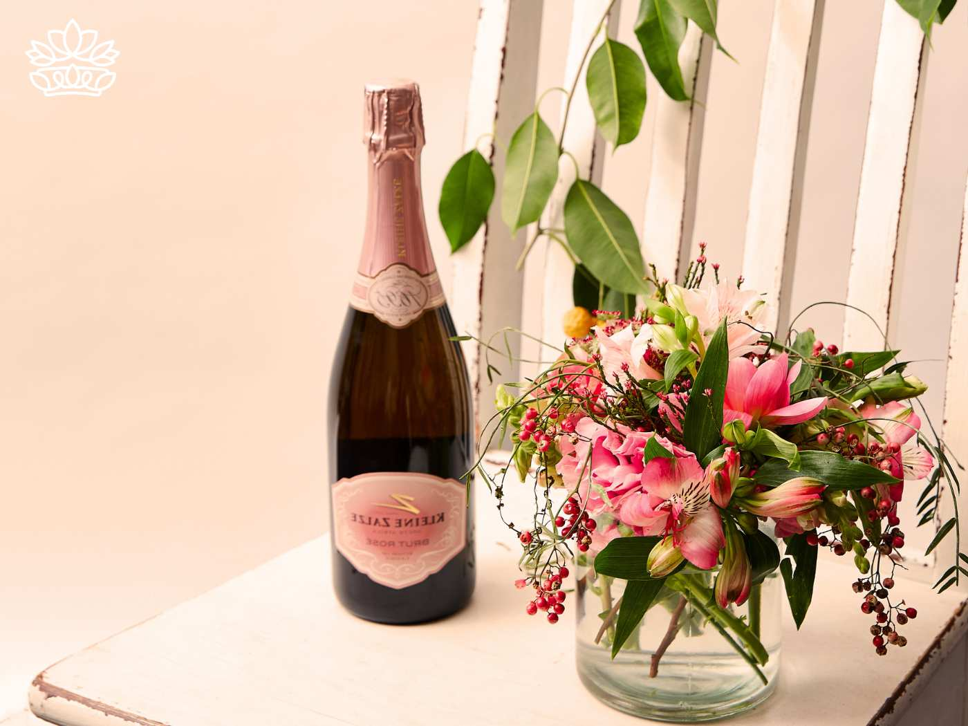 A bottle of rosé champagne and a bouquet of vibrant pink flowers on a white chair. Flowers with Champagne & Wine. Delivered with Heart. Fabulous Flowers and Gifts.