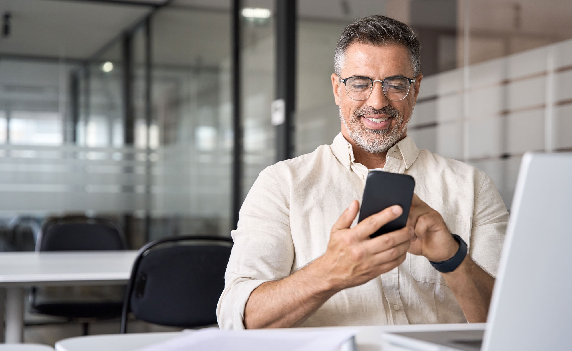 Smiling insurance professional using a mobile device in a modern office, showcasing mobile-friendly features of insurance agency management systems.