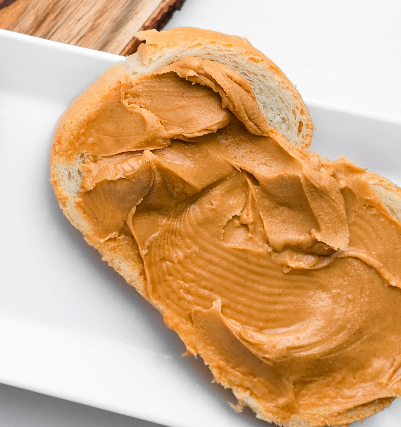 A close-up of peanut butter on a slice of bread on a white plate.