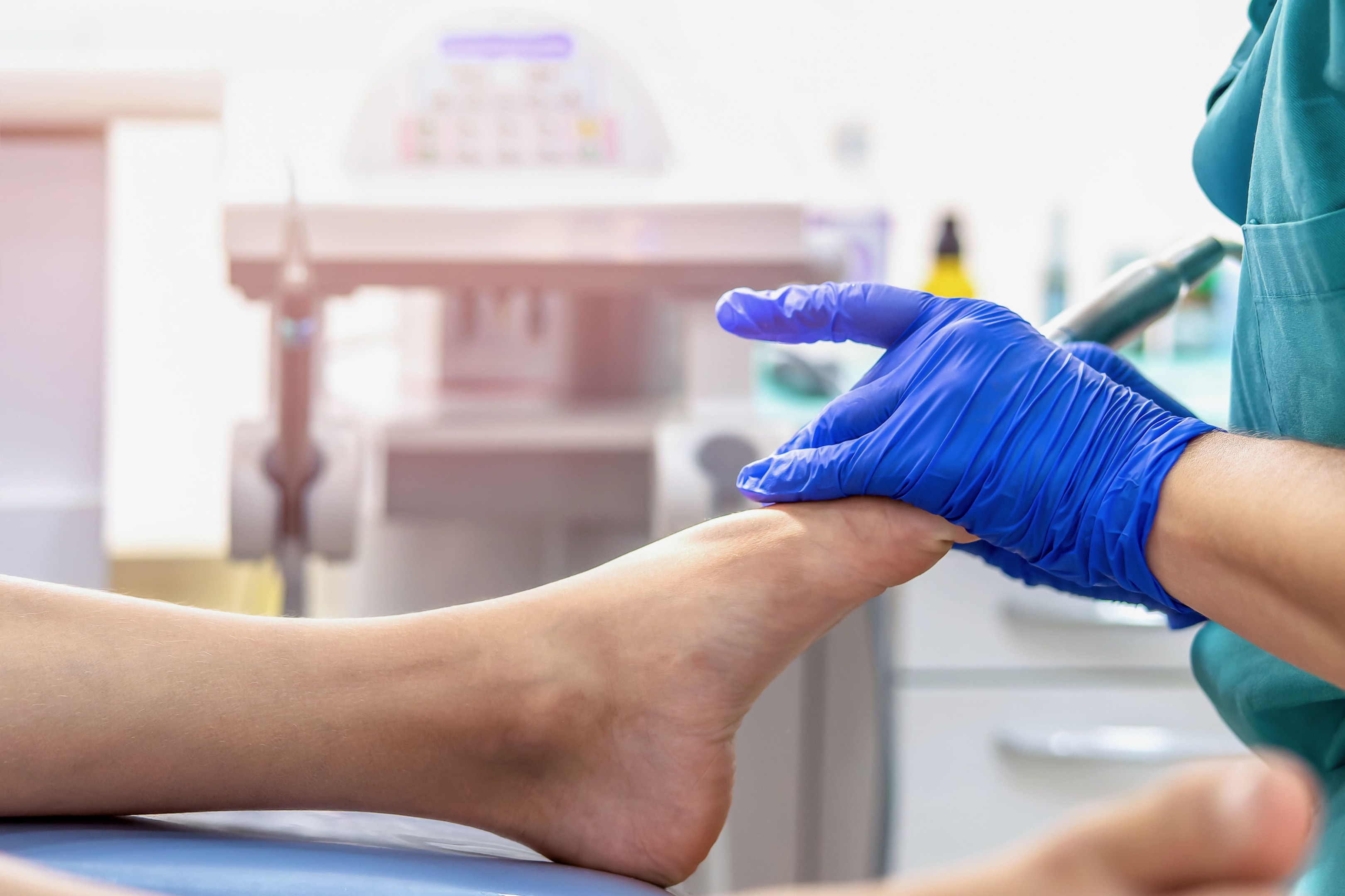 Clinician wearing blue gloves examines a patient’s ankle and foot in a clinic, checking pain and mobility during peroneal tendonitis recovery time.