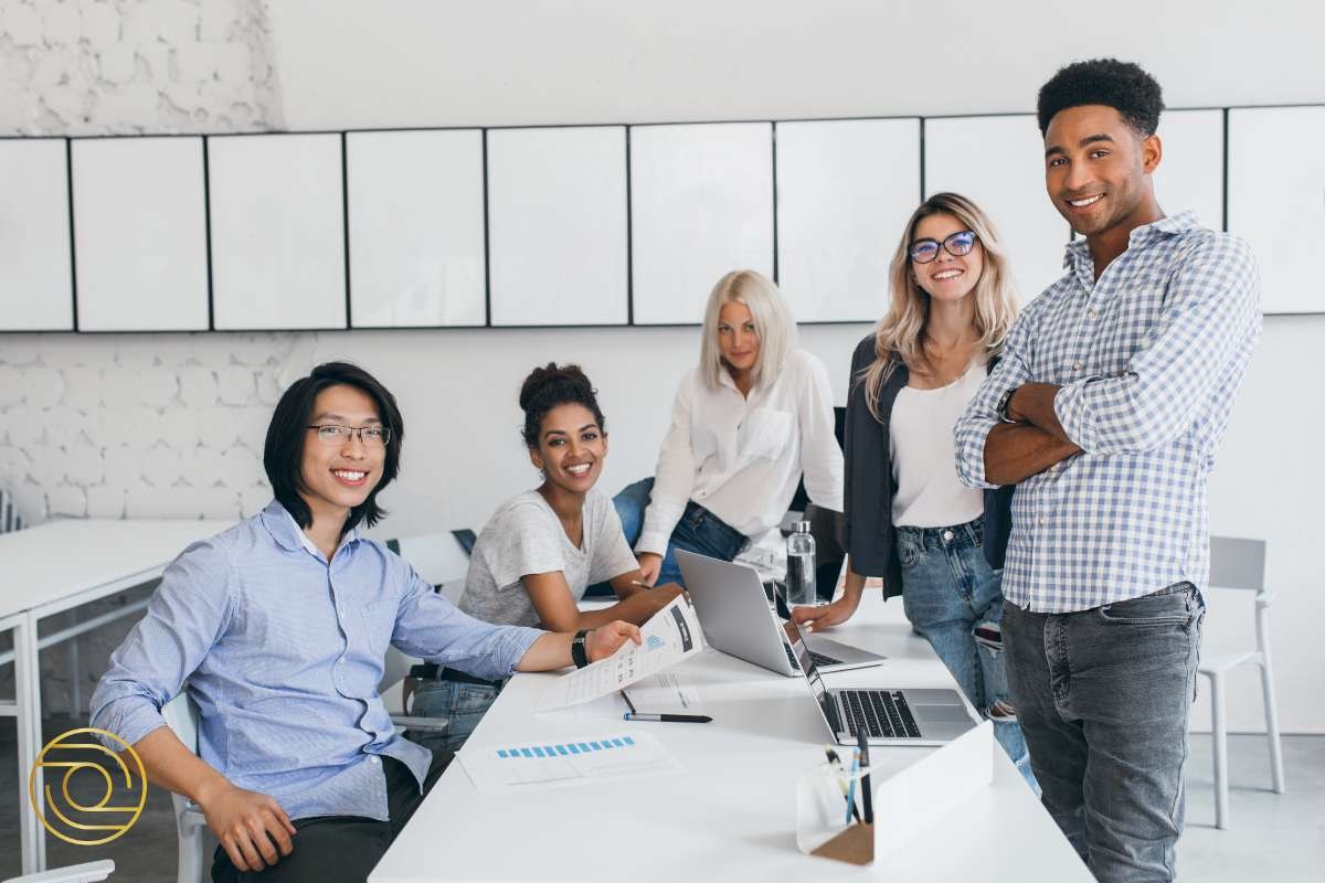 Five team members pose confidently in a shared office space, exemplifying a strengths based approach to leadership. This group showcases effective collaboration, mutual trust, and newly developed skills from a recent team building activity, highlighting how understanding unique strengths, setting goals, and building relationships can lead to a more successful future in the business world.