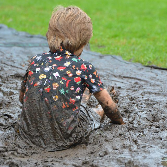 Young child sitting and playing in a giant mud puddle