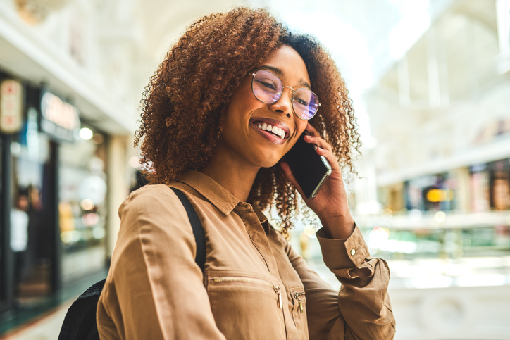 Cheerful young woman with beautiful curls talking on her cell phone in a mall.