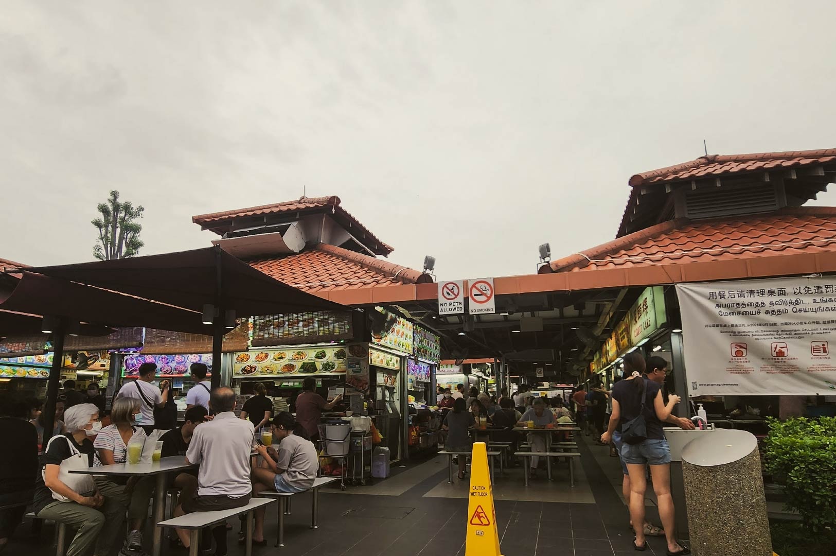 Chomp Chomp Food Centre outdoor dining with wet floor sign, no smoking notice, and busy food stalls serving local dishes.