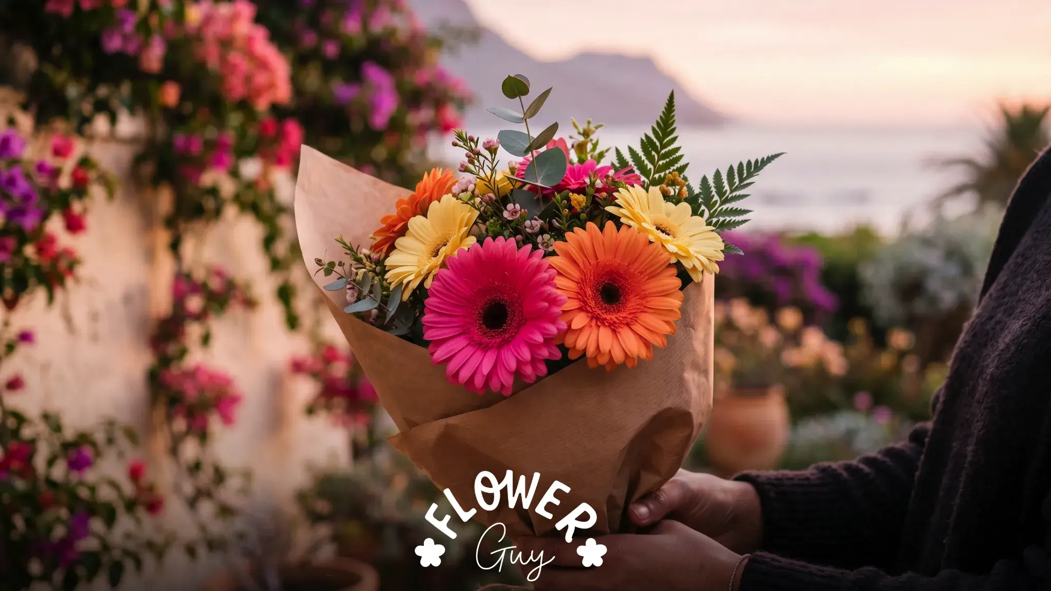 Hands holding a small bunch of pink, orange and yellow gerbera daisies wrapped in kraft paper at dawn in a Cape Town garde