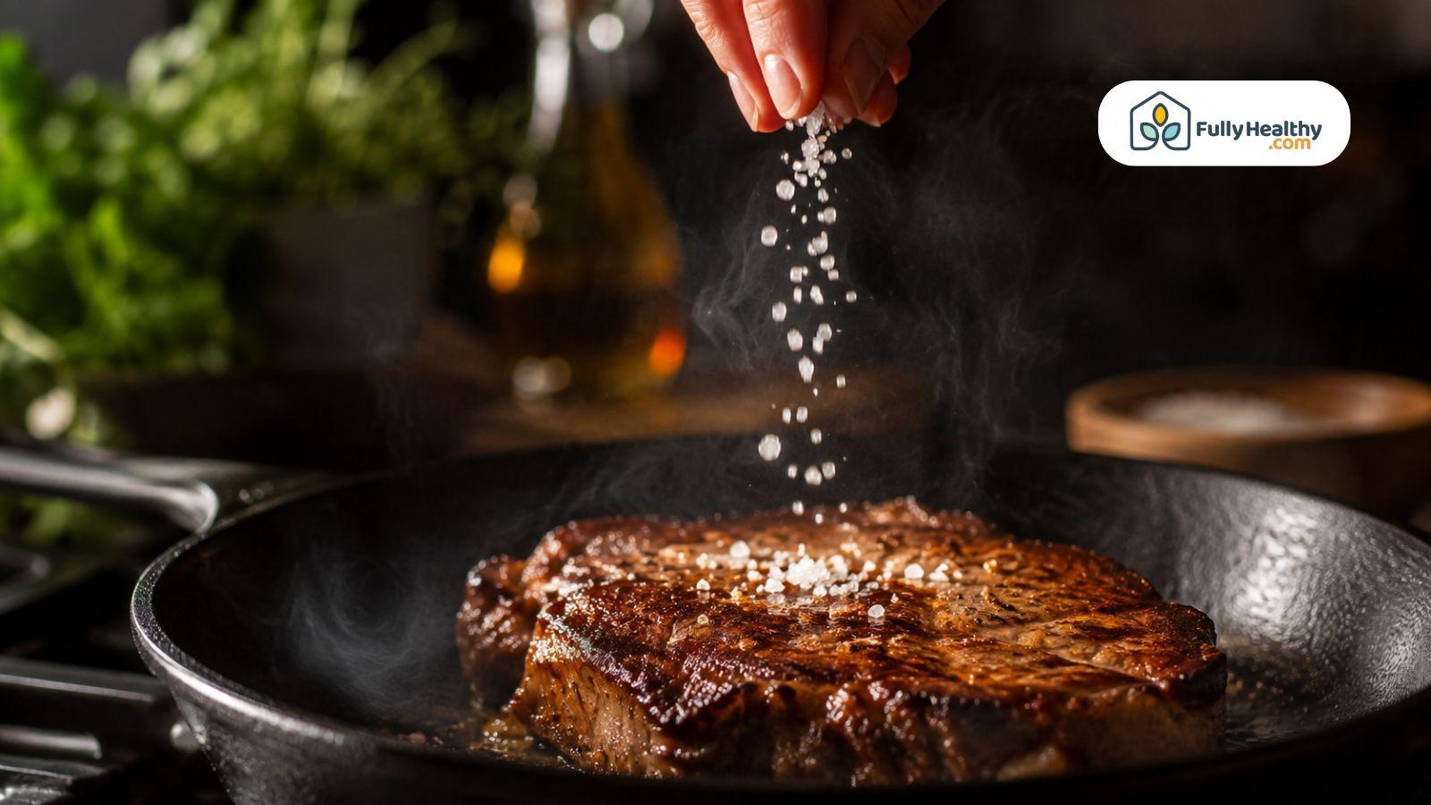 Hand sprinkling coarse kosher salt onto sizzling steak in cast iron skillet.