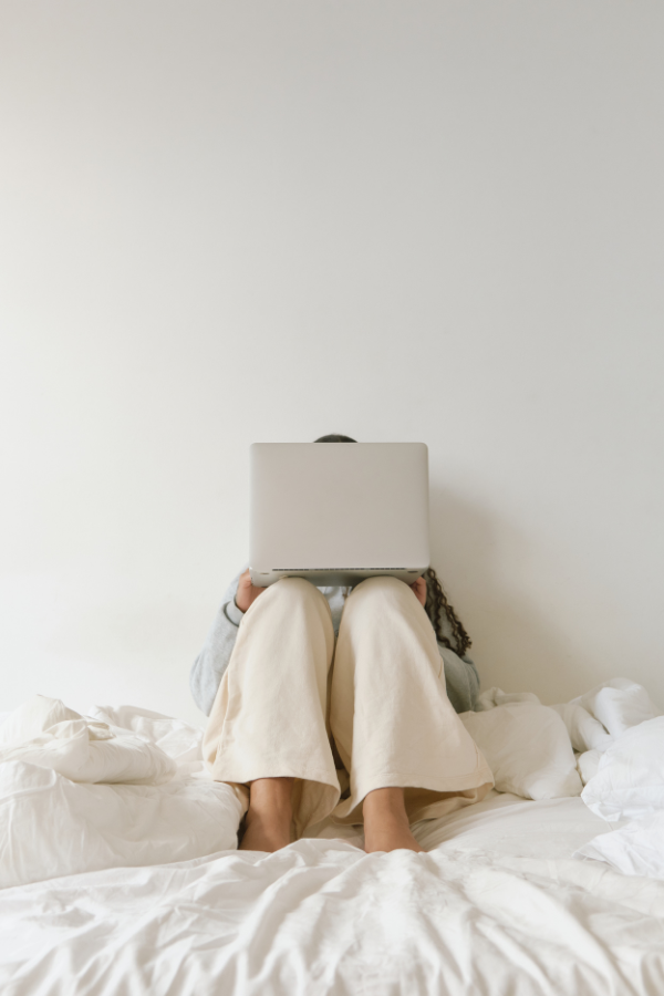 a woman sits on her bed using a laptop