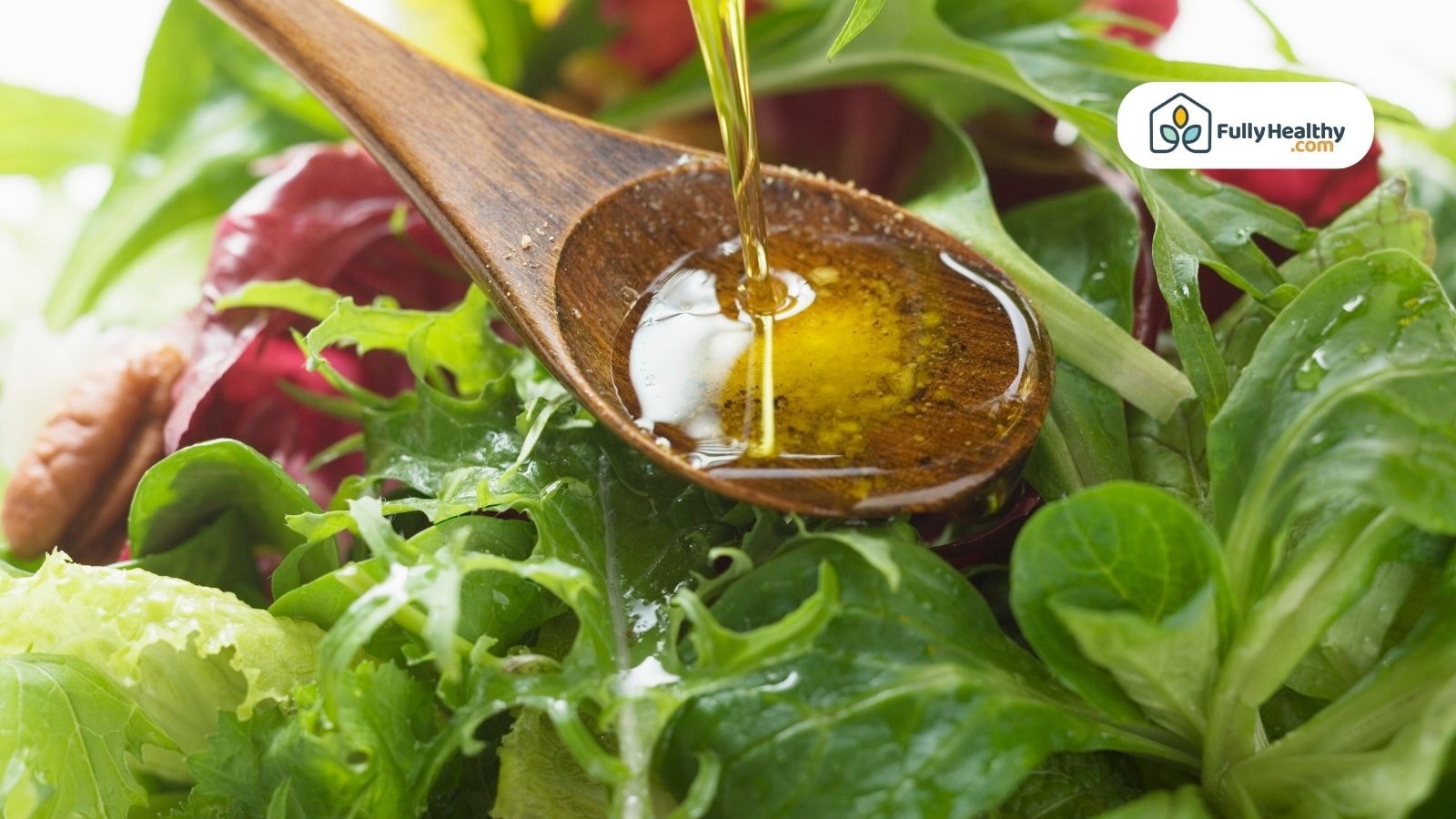 Olive oil being poured over fresh salad greens from a wooden spoon.