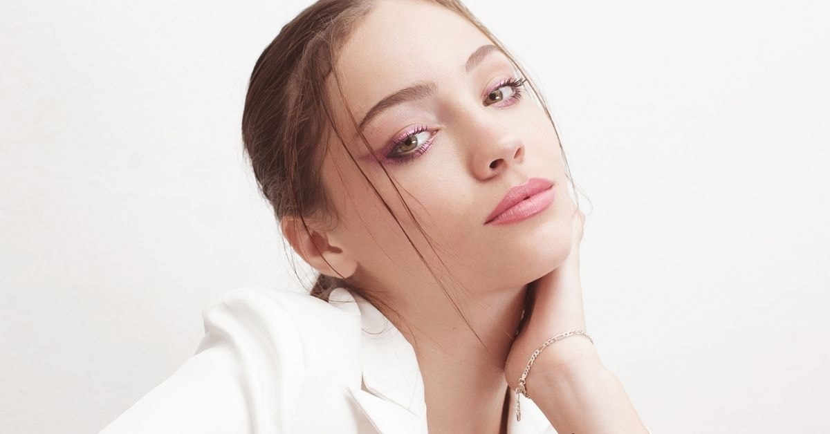 Young woman with pink makeup and soft smile, promoting a fast tax service, posing with hand on her face.