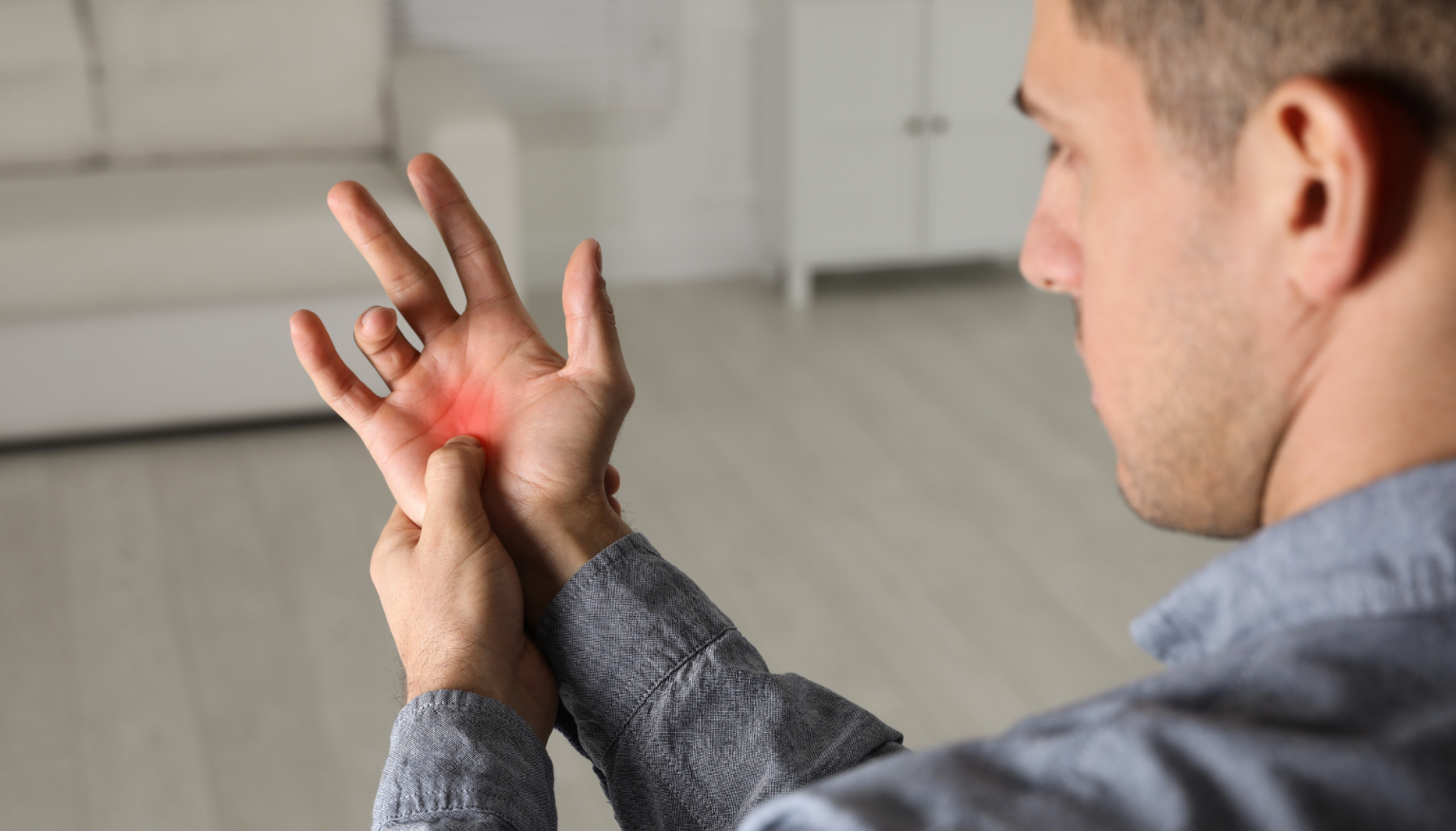 En mann holder håndleddet sitt med den andre hånden, med synlig rødhet i håndflaten som tegn på smerte eller betennelse.