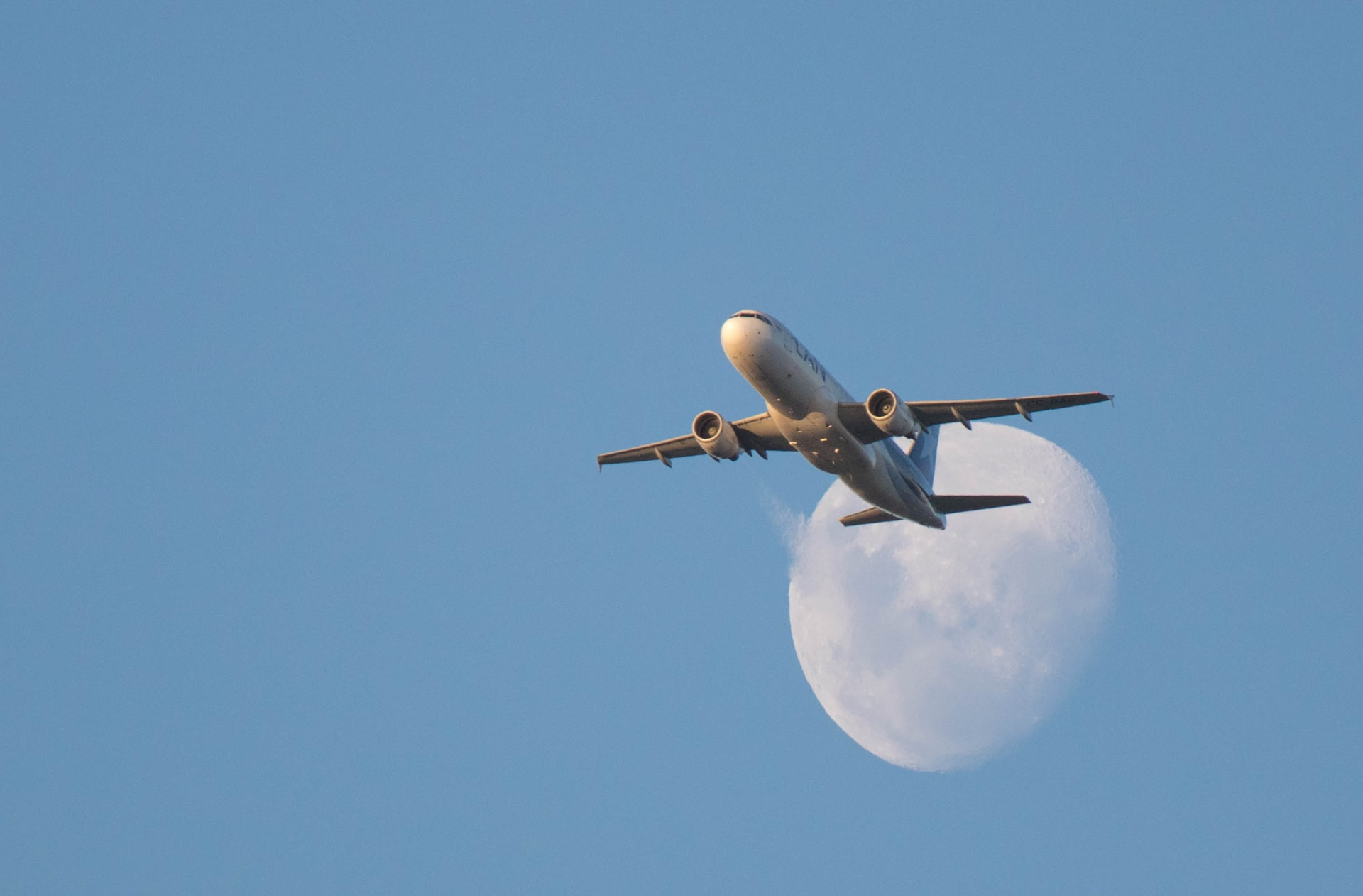 A standard commercial aircraft taking off with moon in the background.