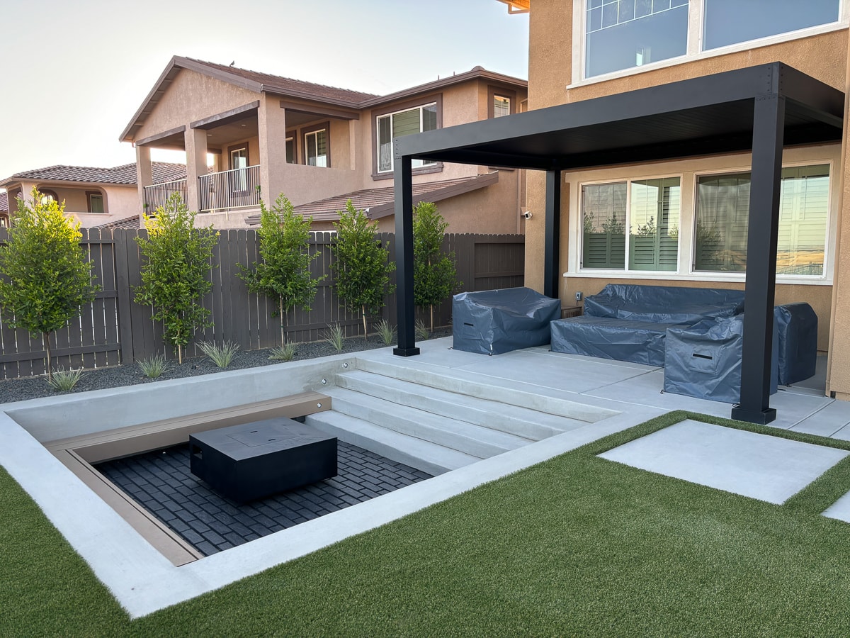Sunken seating area with natural gas fire pit installed next to a luxury pergola.